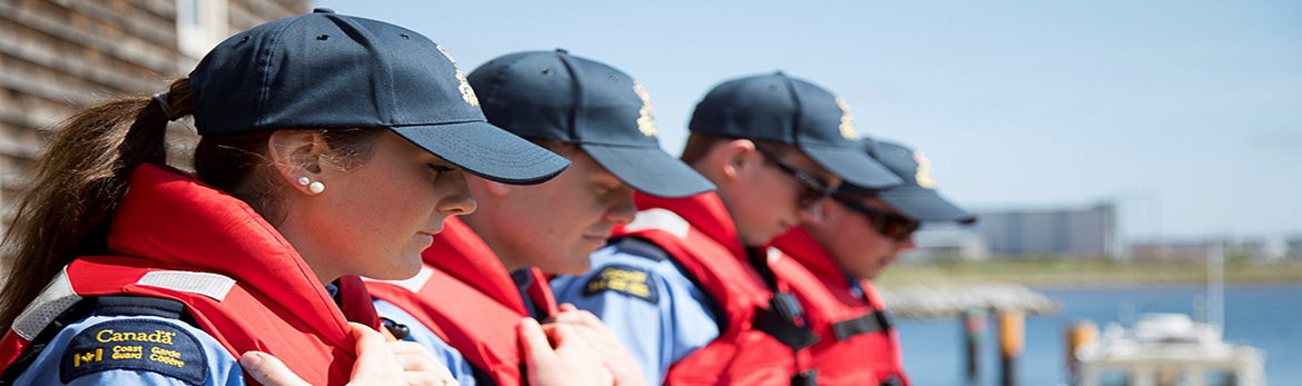 Officer cadets in life jackets, standing by the waterfront.